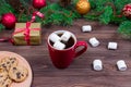 Red cup of tea with white marshmallows with cookies on a wooden table against the background of a Christmas tree with Royalty Free Stock Photo