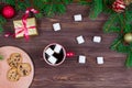 Red cup of tea with white marshmallows with cookies on a wooden table against the background of a Christmas tree with Royalty Free Stock Photo