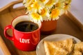 Red cup with the word `love` with hot coffee / tea, a bouquet of daisies and pancakes with honey on a wooden tray Royalty Free Stock Photo