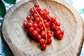 Red currant branch on wooden plate with gentle background. Beautiful berries bunch on beige cutting board. Fruit plate, bowl.