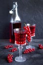 Red currant drinks in a beautiful glass goblets with bottle of currant drink on dark grey surface. Bunches of red currants on