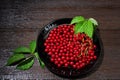 Red currants with leaves in a black bowl on a wooden background. Harvest of ripe summer berries. Closeup Royalty Free Stock Photo