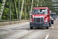 Red day cab big rig semi truck transporting liquid cargo in tank semi trailer driving on the highway road with truss bridge Royalty Free Stock Photo