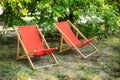 Red Deckchairs in autumn garden. Two deckchairs on summer green lawn. Lounge sunbed. Wooden garden furniture on grass lawn outdoor