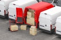 Red delivery van with open doors and hand truck with cardboard boxes iin a row of white vans. Delivery and shipping concept Royalty Free Stock Photo