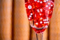 Red dice in a glass of champagne on a background of yellow casino chips. Close-up of dice for playing craps, poker