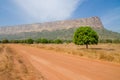 Red dirt and gravel road, single trees and large flat topped mountain in Fouta Djalon region, Guinea, West Africa Royalty Free Stock Photo