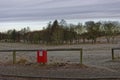 A red Dog Poo bin with sign placed beside a wooden fence Railing, on a pavement by a Frosted fairway of a Golf Club.