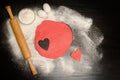 Red dough with a carved heart. Eggs and flour on a black table, rolling pin. Royalty Free Stock Photo