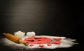 Red dough, cut out hearts, flour, eggs and rolling pin on a black background