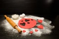 Red dough, cut out hearts, flour, eggs and rolling pin on a black background, space for text