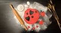 Red dough, cut out hearts, flour, eggs and rolling pin on a black background, space for text