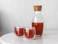 Red drink in elegant carafe and two glass on white table. Bright juice in light background. Compote natural refreshment