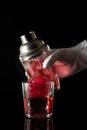 Red drink with ice, bar shaker and bartender`s hand, black background. Royalty Free Stock Photo