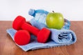 Red dumbbell, fresh water bottle with dew and green apple on blue towel on wooden floor Royalty Free Stock Photo