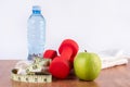 Red dumbbell on towel, green fresh apple and bottle with water and measuring tape on wooden floor Royalty Free Stock Photo