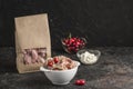 Red dumplings with cherries in a bowl and eco-friendly paper packaging for delivery with white sauce on a dark background