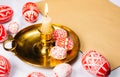 Red Easter eggs with folk white pattern around candlestick with burning candle on paper on white background. Ukrainian traditional