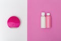 Red electric face brush and cleanser in small bottles on pink and white paper background