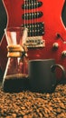 A red electric guitar on a black background, with a coffee brewing jug in front of it and a black coffee mug on coffee beans Royalty Free Stock Photo