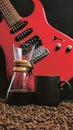 A red electric guitar on a black background, with a coffee brewing jug in front of it and a black coffee mug on coffee beans. Royalty Free Stock Photo