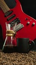 A red electric guitar on a black background, with a coffee brewing jug in front of it and a black coffee mug on coffee beans. Royalty Free Stock Photo