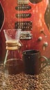 A red electric guitar on a bokeh background, with a coffee brewing jug in front of it and a black coffee mug on coffee beans with Royalty Free Stock Photo