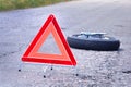 Red emergency triangle stop sign and spare wheel on the road.