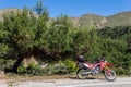 A red enduro motorcycle stands in side of the asphalt road, green nature