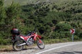 A red enduro motorcycle stands in side of the asphalt road, green nature