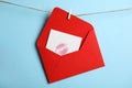 Red envelope and card with lip print hanging on twine against light blue background. Love letter Royalty Free Stock Photo