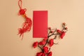 A red envelope, a peach blossom branch and a decorative string are displayed on a minimalist pastel background. Design text on