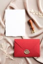 Red envelope with wax seal and blank wedding invitation card mockup on satin fabric. Flat lay, top view, copy space. Wedding Royalty Free Stock Photo