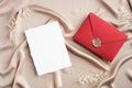 Red envelope with wax seal and blank wedding invitation card mockup on silk fabric. Flat lay, top view, copy space. Wedding Royalty Free Stock Photo