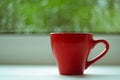 The red espresso cup on white windowsill. On background window and rain. Royalty Free Stock Photo