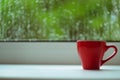 The red espresso cup on white windowsill. On background window and rain. Royalty Free Stock Photo