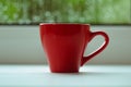 The red espresso cup on white windowsill. On background window and rain. Royalty Free Stock Photo