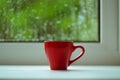 The red espresso cup on white windowsill. On background window and rain. Royalty Free Stock Photo