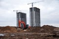 Red excavator with bucket at building under construction. Backhoe at large scale construction site against tower cranes. Royalty Free Stock Photo