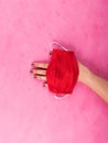 Red face mask in female hand on pink. Covid-19 Royalty Free Stock Photo