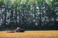 Red farming tractor is working in the field. Disc harrow for crushing stubbles.