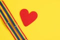 red felt heart and two bracelets with lgbt colors on yellow background copy space top view, pride concept