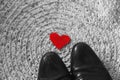 Red felt heart under men`s black shoes on crochet carpet background - symbolizes relationship of unrequited love