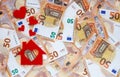 Red felt small house with heart-shaped window and red hearts above on 50 fifty euro banknotes background.