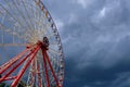 Red Ferris wheel against a gray cloudy sky.