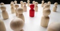 Red figure surrounded by white wooden figurines on table