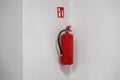 Red fire extinguisher hanged on a white wall near corner with a sticker Royalty Free Stock Photo