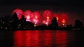 Red Fireworks light up the night sky over a city skyline with river reflections Royalty Free Stock Photo