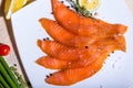 Red fish sliced in slices lies on a white plate. Around vegetables and slivers