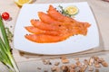 Red fish sliced in slices lies on a white plate. Around vegetables and slivers